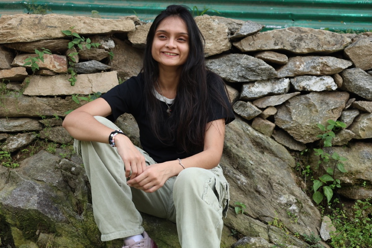Anushka smiling, sitting on a stone wall outdoors